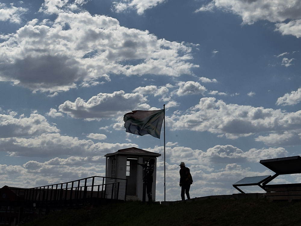 Albie silhouetted next to flag on Old Fort Prison ramparts at ConCourt